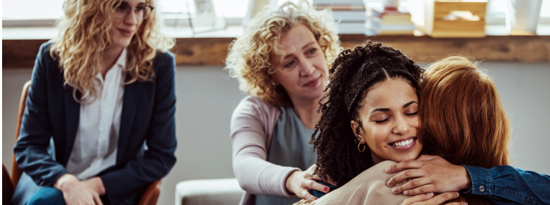 Woman hugging and comforting another woman at adult behavioral addiction therapy